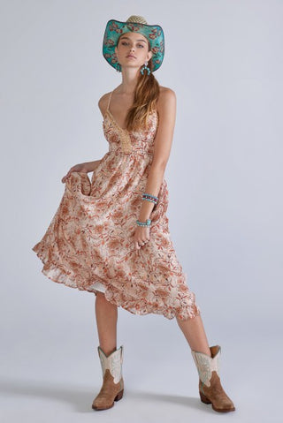 Ärmelloses, fließendes Kleid mit rosa Blumenmuster und türkisfarbenem Hut, kombiniert mit braunen Stiefeletten.