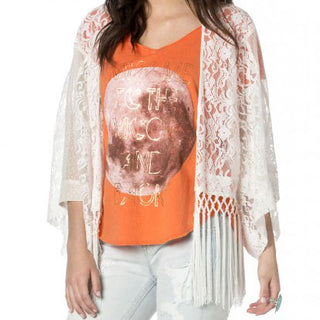 Weißer Spitzenkimono mit langen Fransen über orangefarbenem Shirt und heller Jeans.