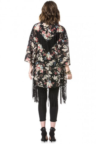 Schwarzer Kimono mit buntem Blumenmuster und langen Fransen, über schwarzer Jeans getragen.