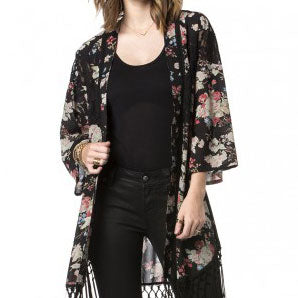 Schwarzer Kimono mit buntem Blumenmuster und Fransen über schwarzem Shirt und Jeans.